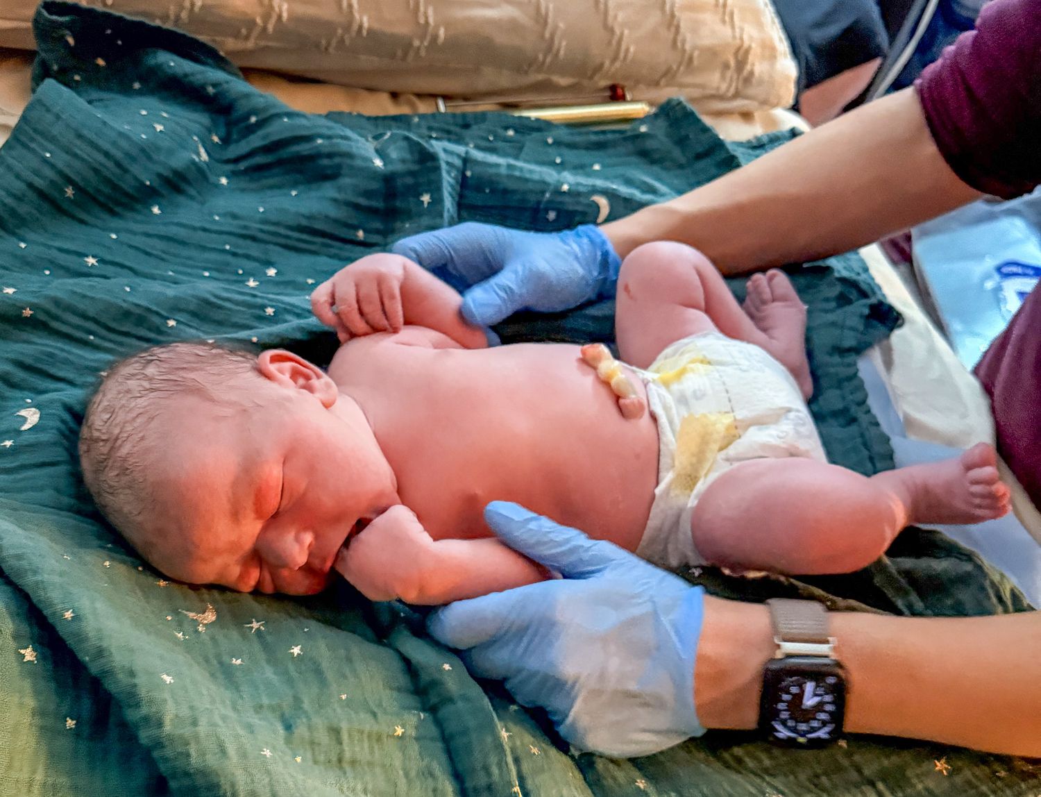 Newborn baby lying on a green blanket being examined by a midwife.