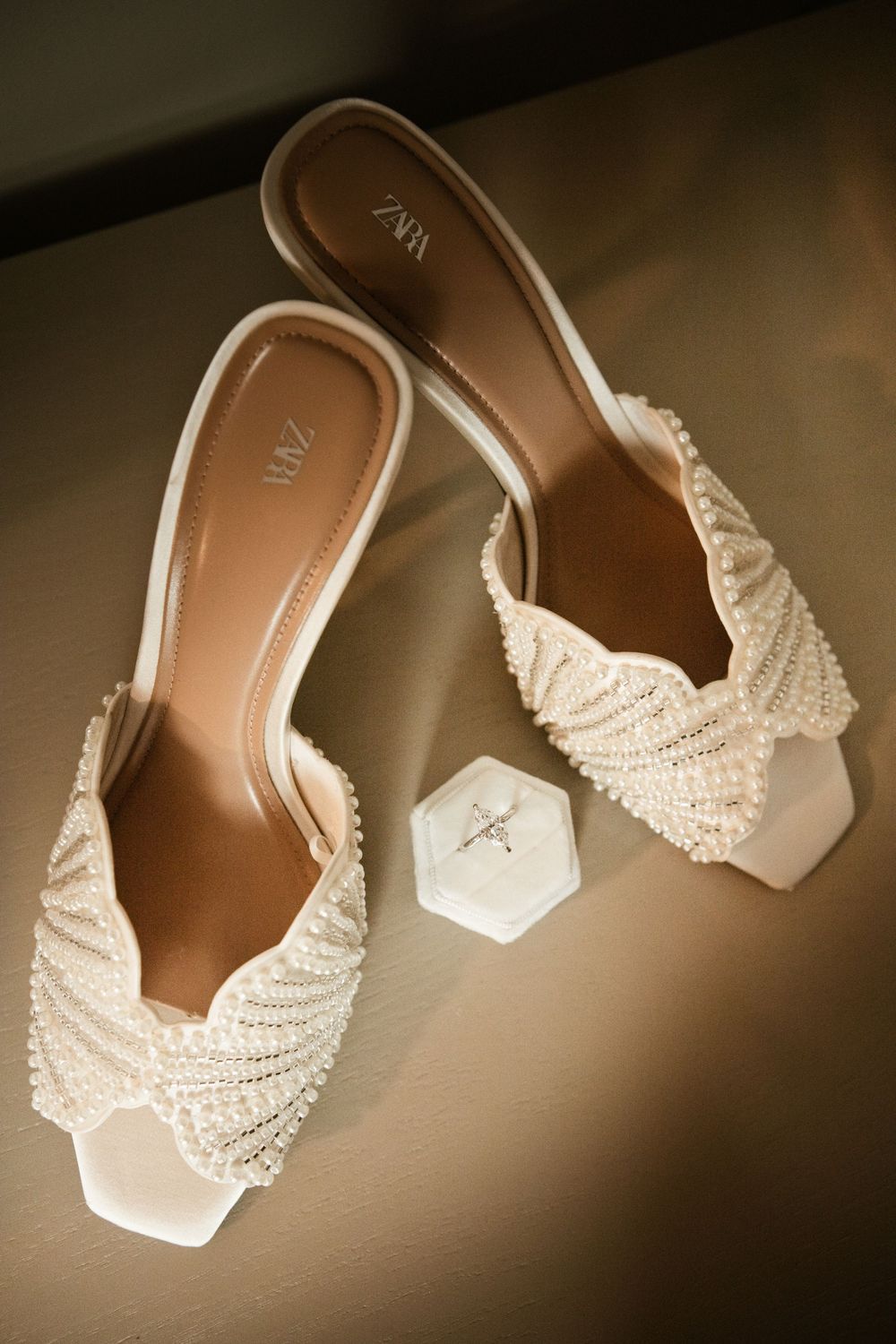 Pearl-embellished Zara bridal heels displayed beside a diamond ring box on a dark surface.
