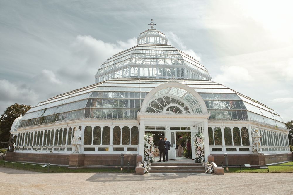 Stunning Victorian glass greenhouse wedding venue with arched windows under a dramatic cloudy sky.