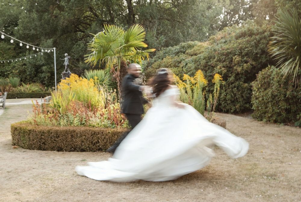 Bride and groom share a joyful spinning dance outdoors in an autumn botanical garden.