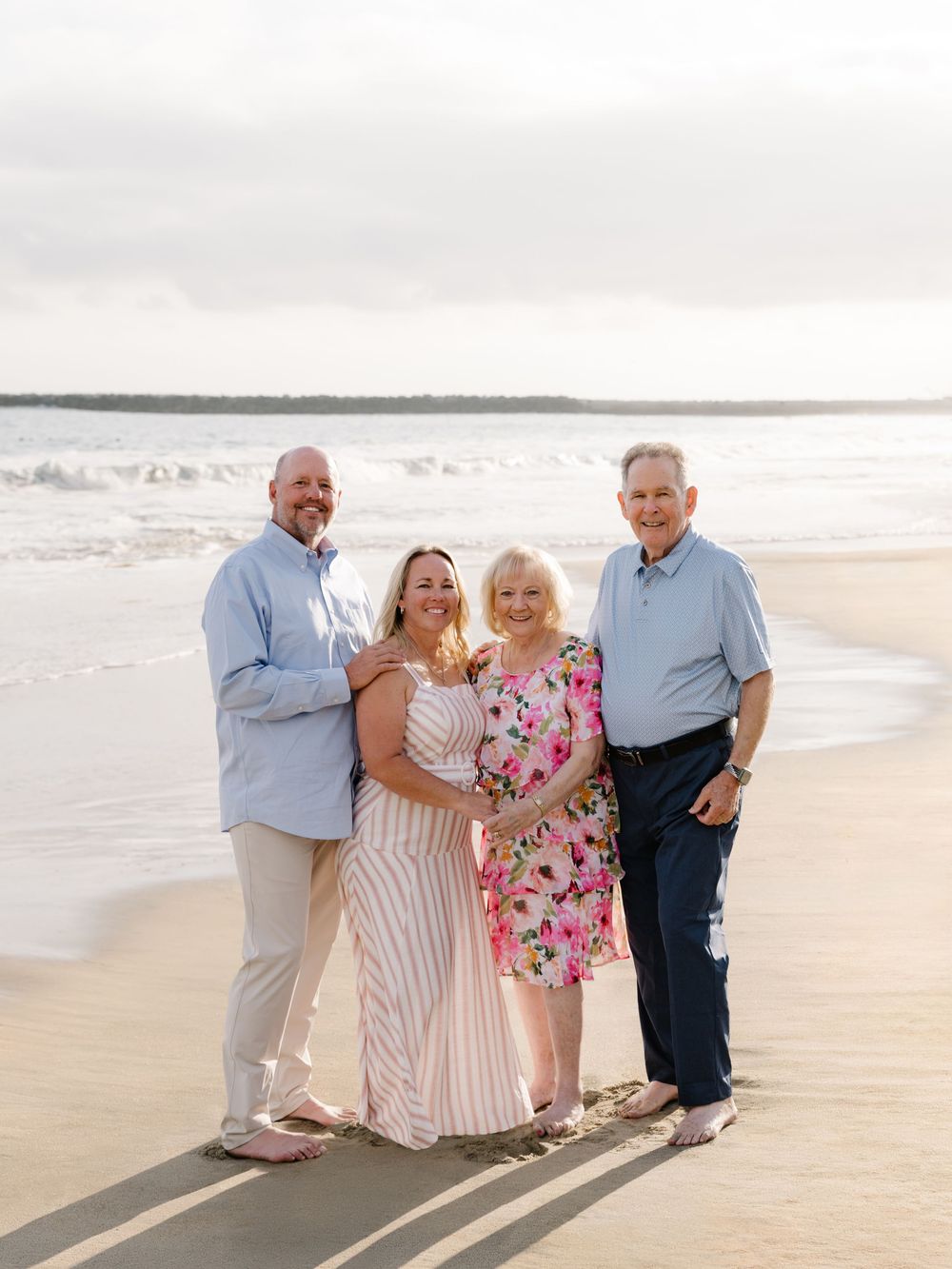 Older couple standing with family members on the beach during a 56th wedding anniversary photo session in Newport Beach.