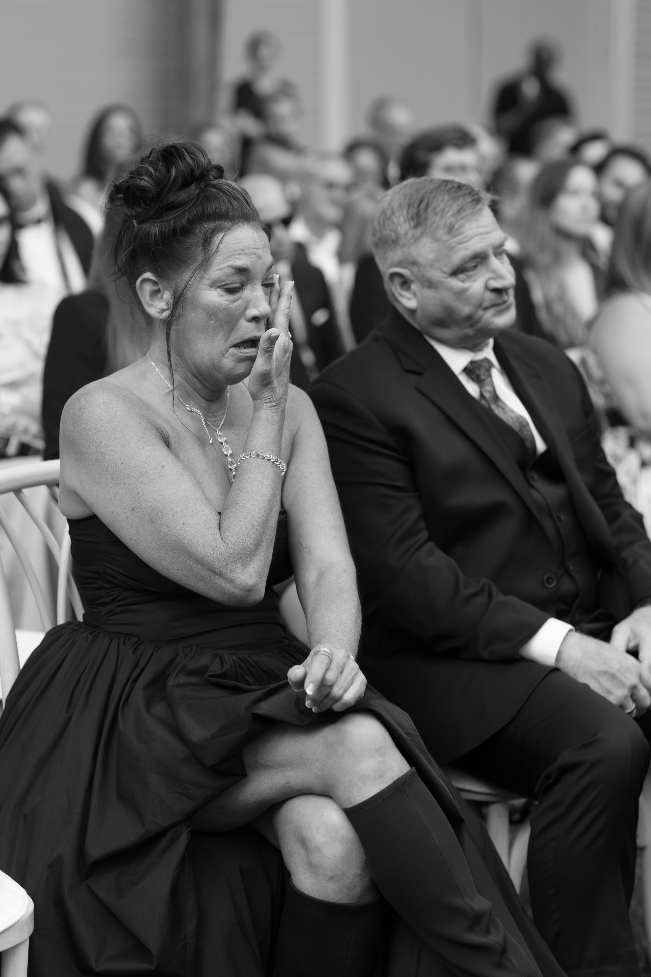 Black and white photo of emotional woman wiping tears at a formal event, seated beside a man in a suit.