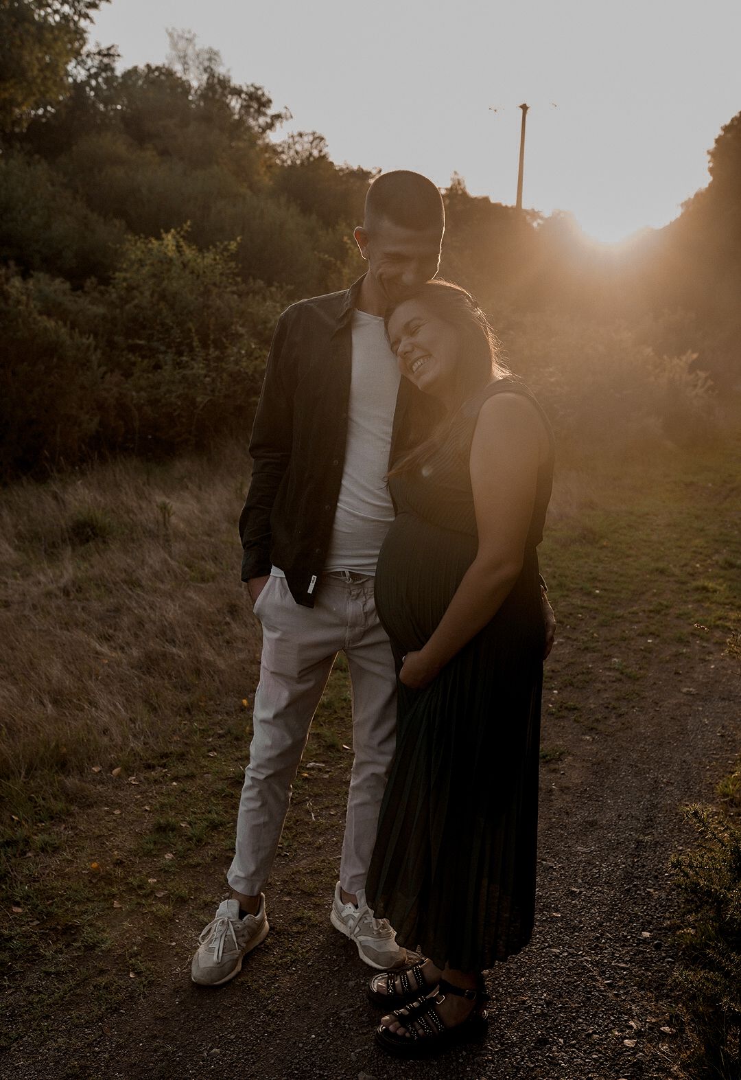 Couple avec femme enceinte s'embrassant sur le chemin rural pendant l'heure dorée du coucher du soleil en Bretagne.