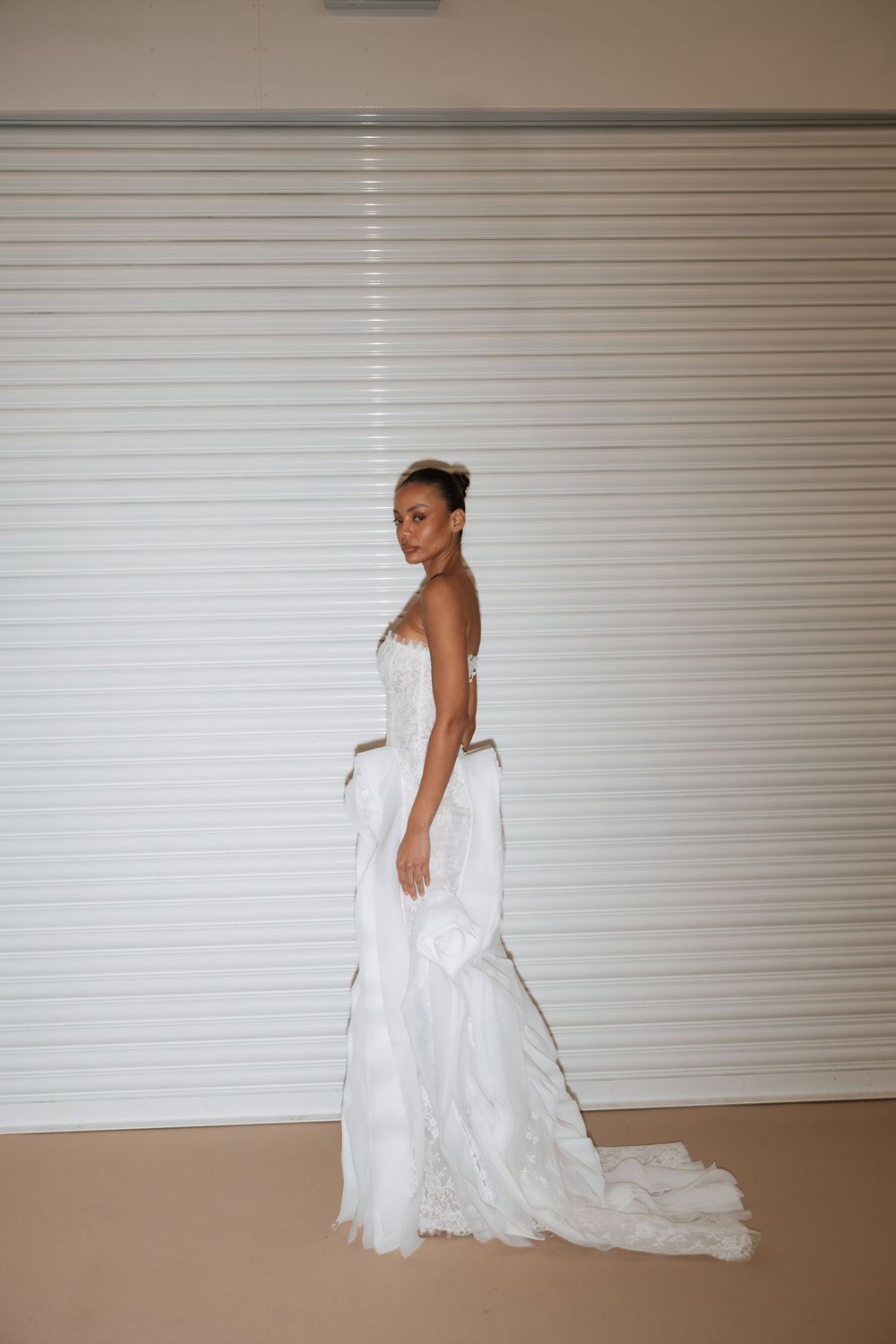 A model poses in an elegant strapless white bridal gown with a flowing train against a white backdrop.