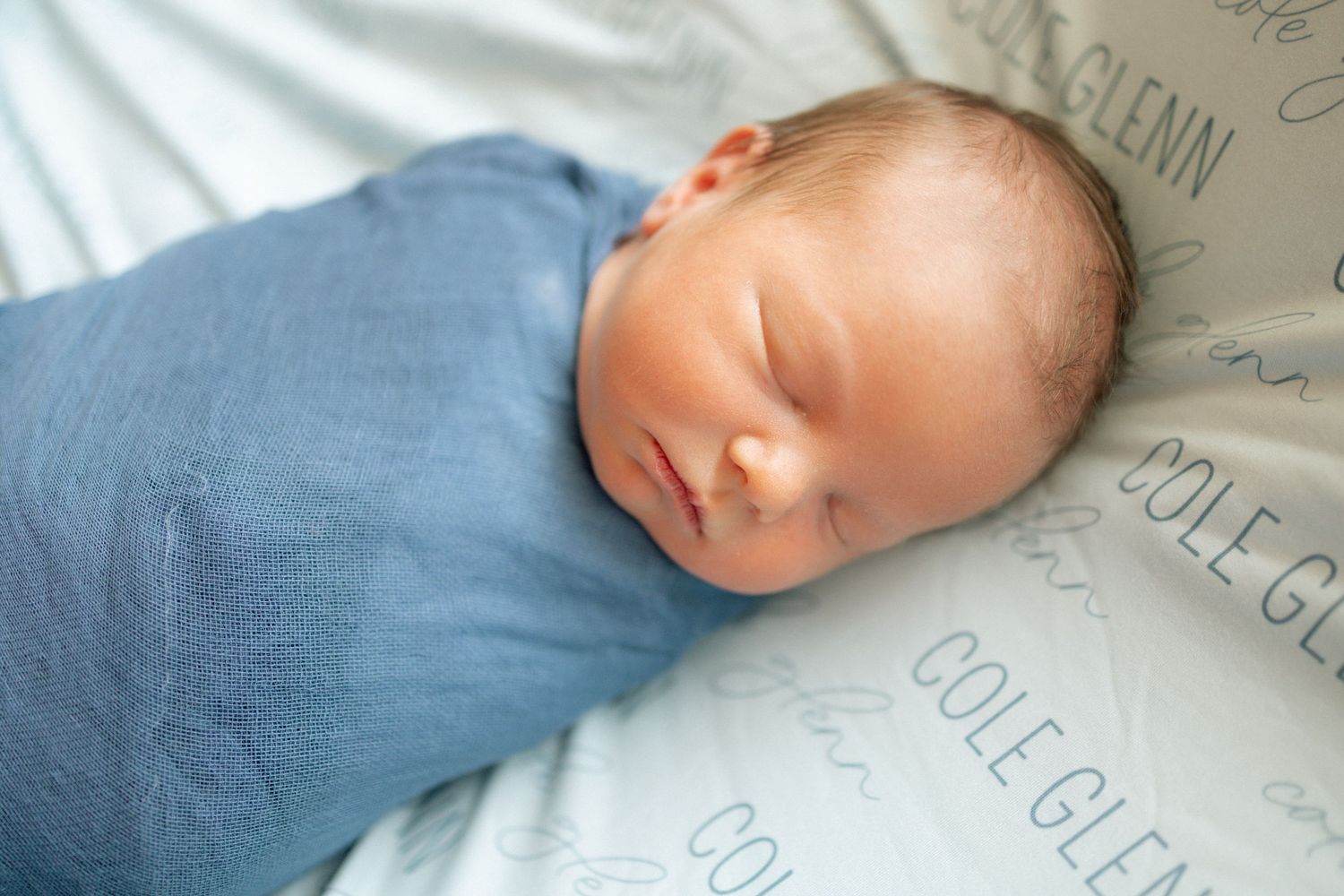Newborn baby swaddled in blue wrap sleeping peacefully on personalized blanket with Cole Glenn name print at University of Tennessee.