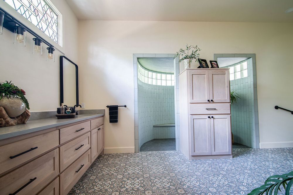 Spacious bathroom with wood vanity, patterned tile floors, and walk-in shower with green tile walls.