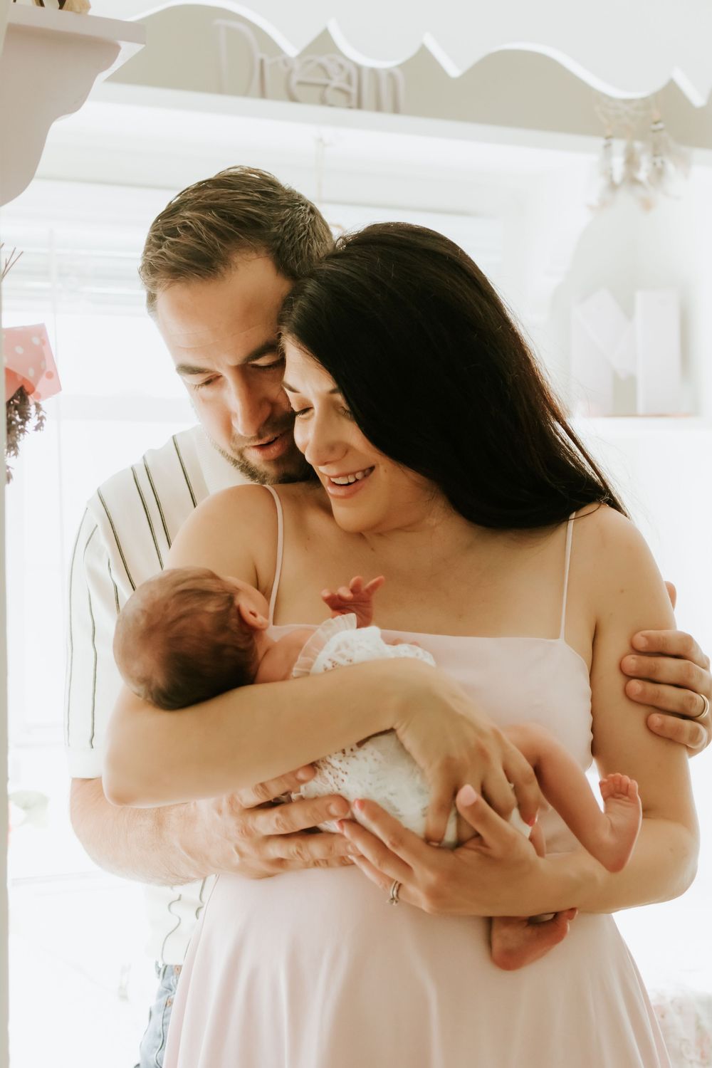 New parents tenderly cradling their newborn baby together in a bright nursery room.