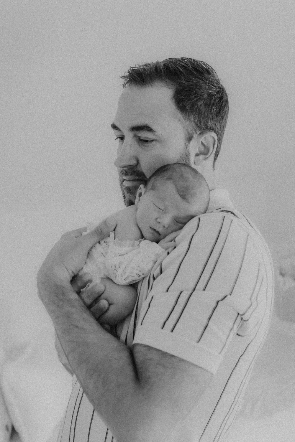 Black and white photo of a bearded father tenderly holding his sleeping newborn baby close to his chest.