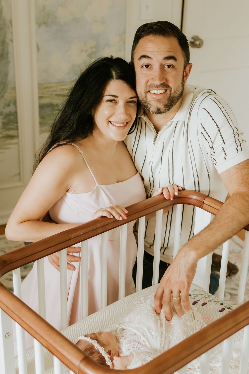 Happy couple smiling over a baby crib with their newborn during an in-home lifestyle newborn photography session.
