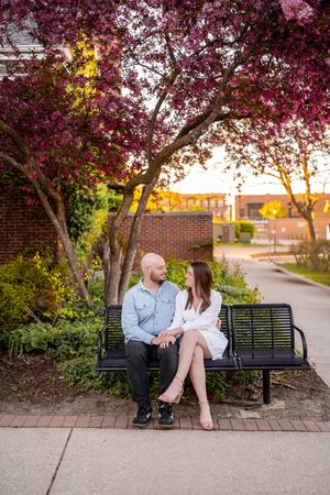 Couple sitting on a black bench under blooming pink trees at sunset in a charming outdoor setting.