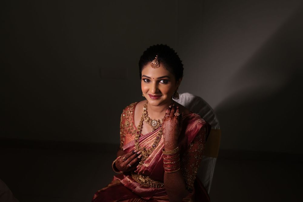 Indian bride in red saree and gold jewelry smiling gracefully in dramatic studio lighting.