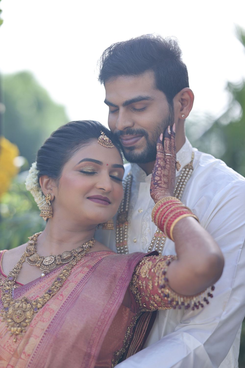 Indian bride and groom in traditional wedding attire, bride wearing gold jewelry and mehndi, groom in white kurta.