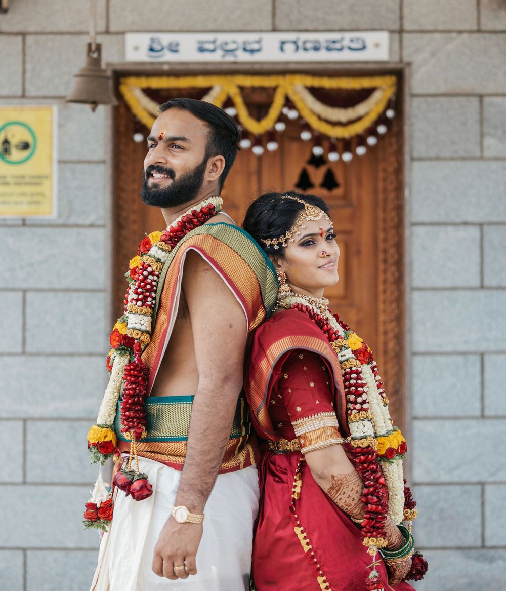 South Indian couple in traditional wedding attire standing back-to-back outside a decorated temple.