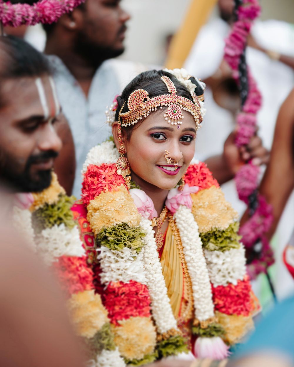 South Indian bride adorned with colorful flower garlands and traditional bridal jewelry during wedding ceremony.
