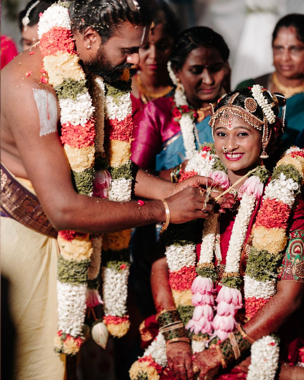 South Indian groom and bride exchanging garlands during traditional Hindu wedding ceremony with guests.