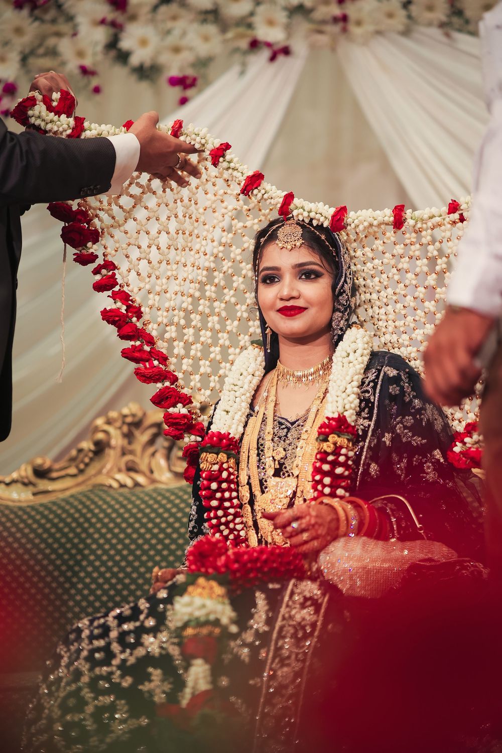 Muslim bride in dark bridal attire holding flower garland during traditional nikah wedding ceremony.