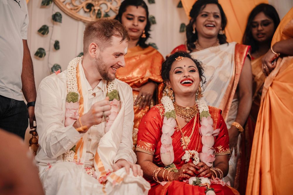 Joyful intercultural wedding ceremony with laughing bride in red saree and Western groom in traditional attire.