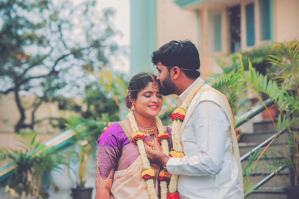 South Indian bride and groom sharing a tender moment outdoors, bride wearing white saree with floral garland.