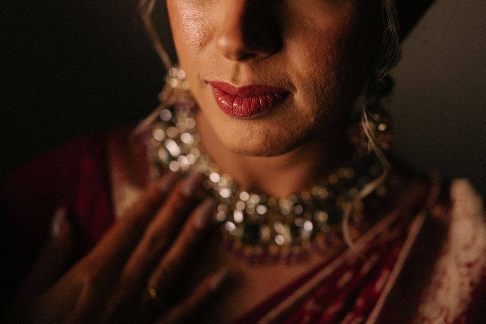 Close-up of Indian bride wearing ornate silver jewelry and red lipstick in traditional bridal attire.