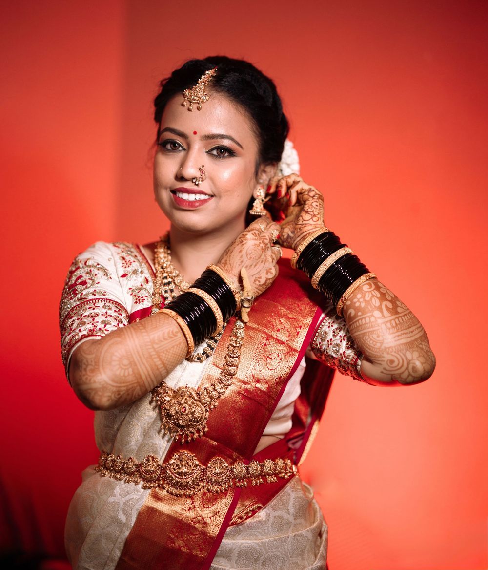 South Indian bride in white and red silk saree adjusting earrings with mehndi-adorned hands.