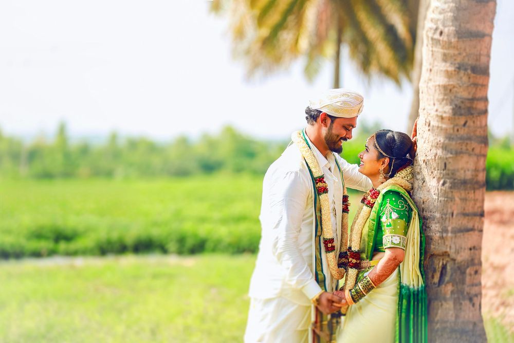 Indian wedding couple sharing romantic moment near palm tree with lush green fields in background.