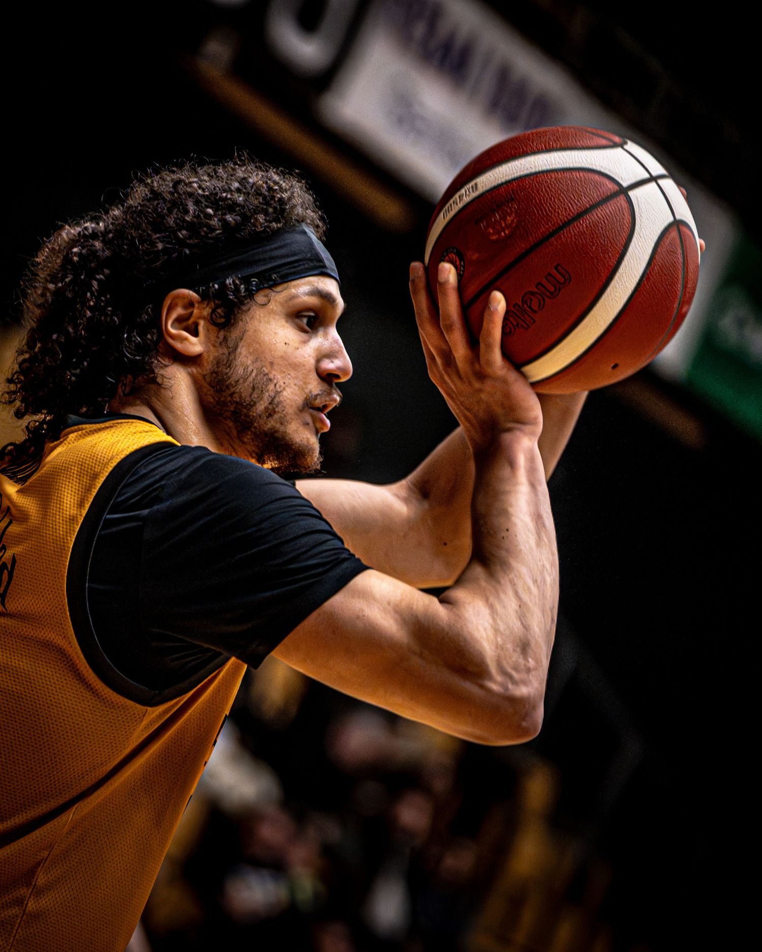 A basketball player in a yellow jersey holds a ball in shooting position during an indoor game.