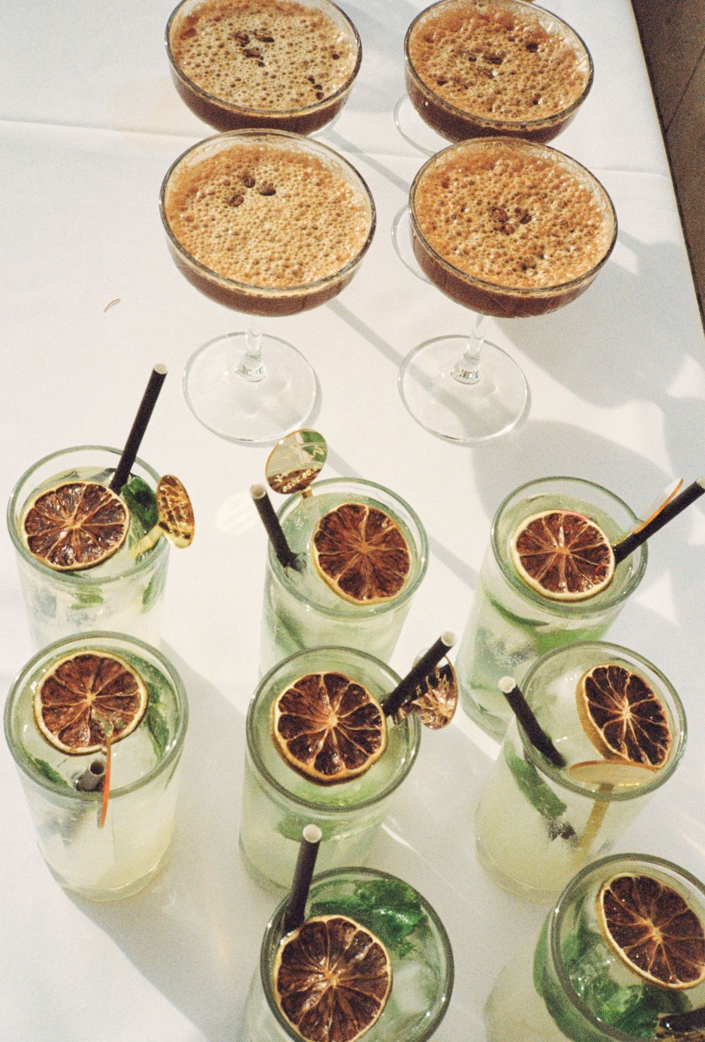 Elegant cocktail display with espresso martinis and citrus garnished mojitos on a white table.