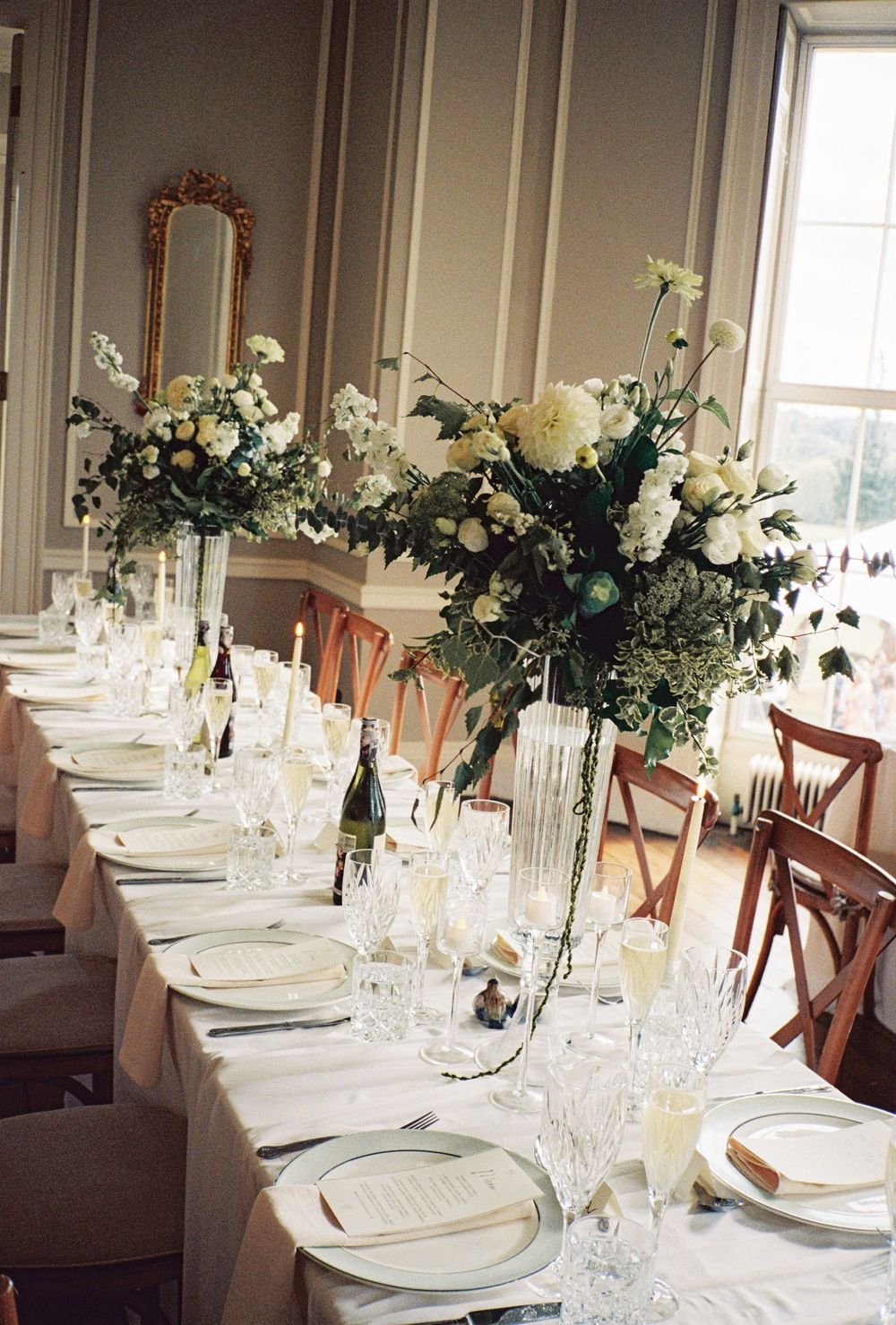 Elegant wedding reception table with white floral centerpieces, crystal glassware, and white linens in a classic venue.