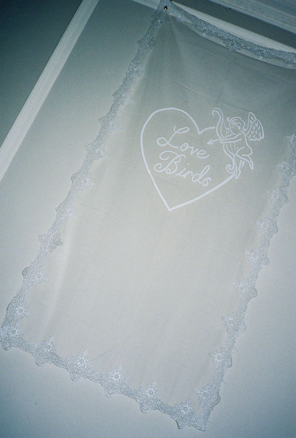 Sheer white fabric panel with lace trim edges and a Love Birds heart graphic design, hung as a decorative curtain.