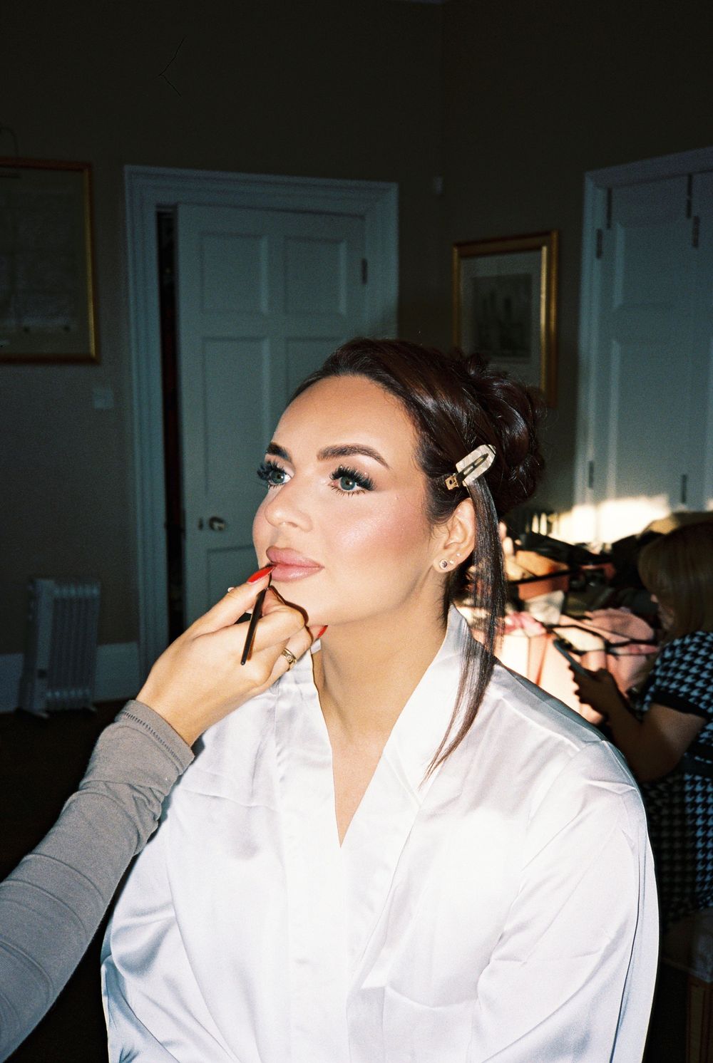 Bride getting lipstick applied by makeup artist during bridal preparation in elegant room.