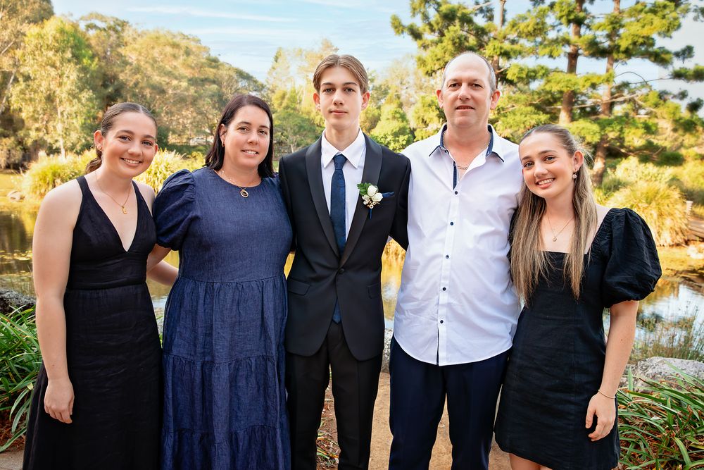 Family of five posing together outdoors at a garden wedding venue, dressed in formal attire.