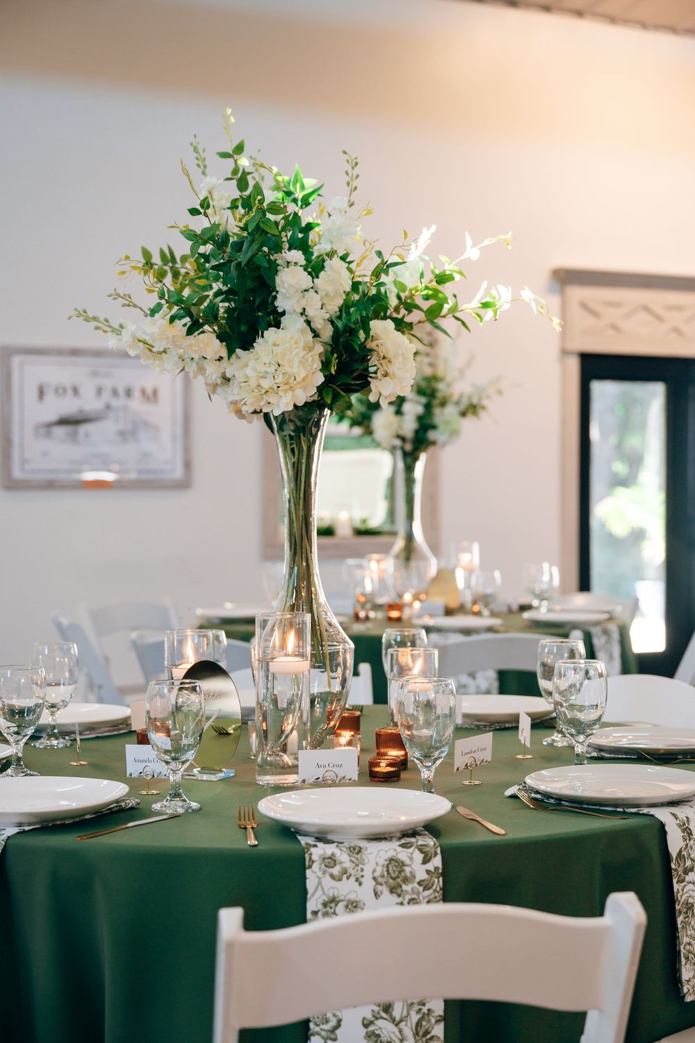 Elegant wedding reception table with green linens, white hydrangea centerpiece, glassware, candles, and place settings.