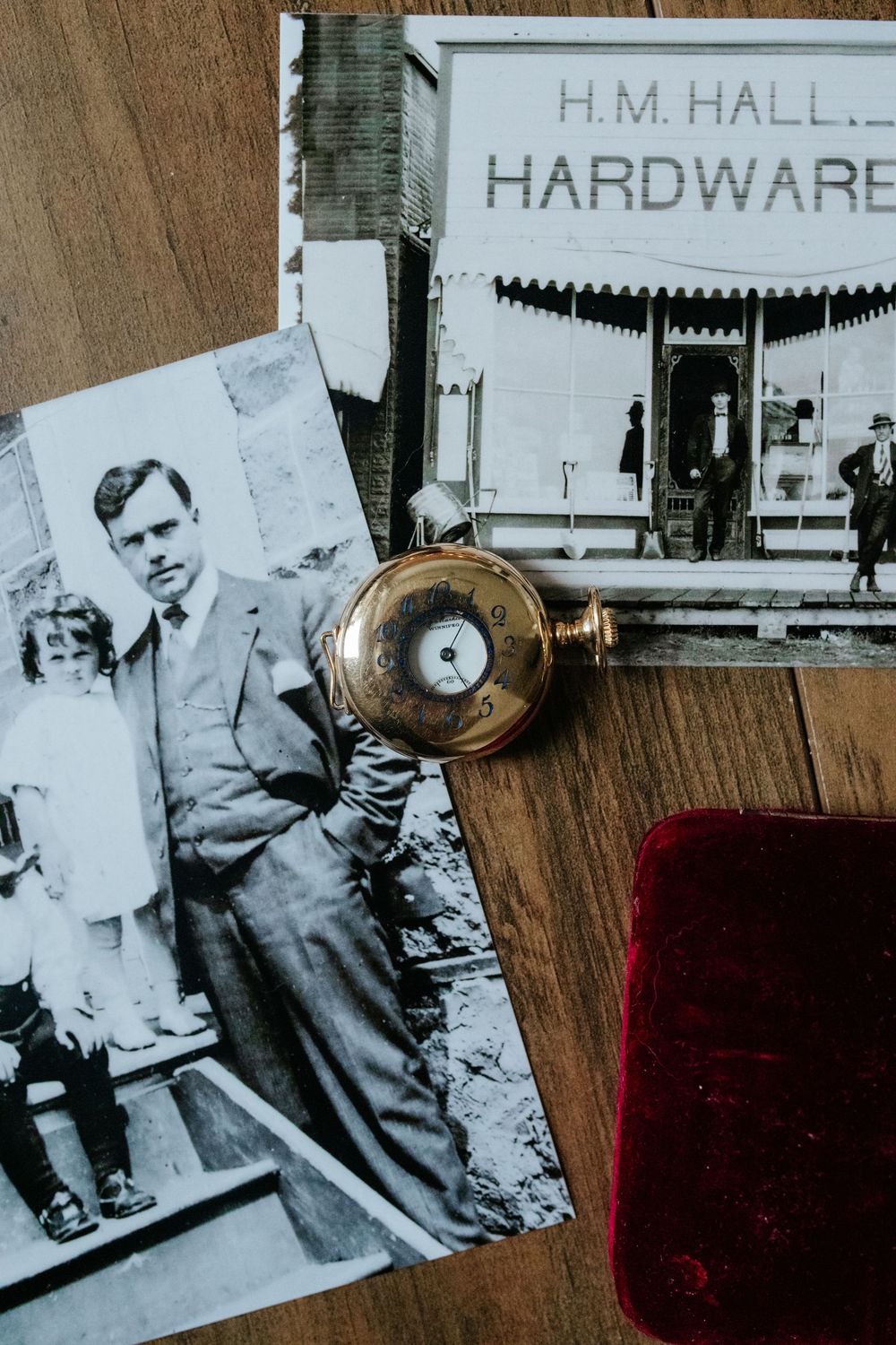 Vintage photographs of a man in a suit and a hardware store beside an antique gold pocket watch on a wooden table.
