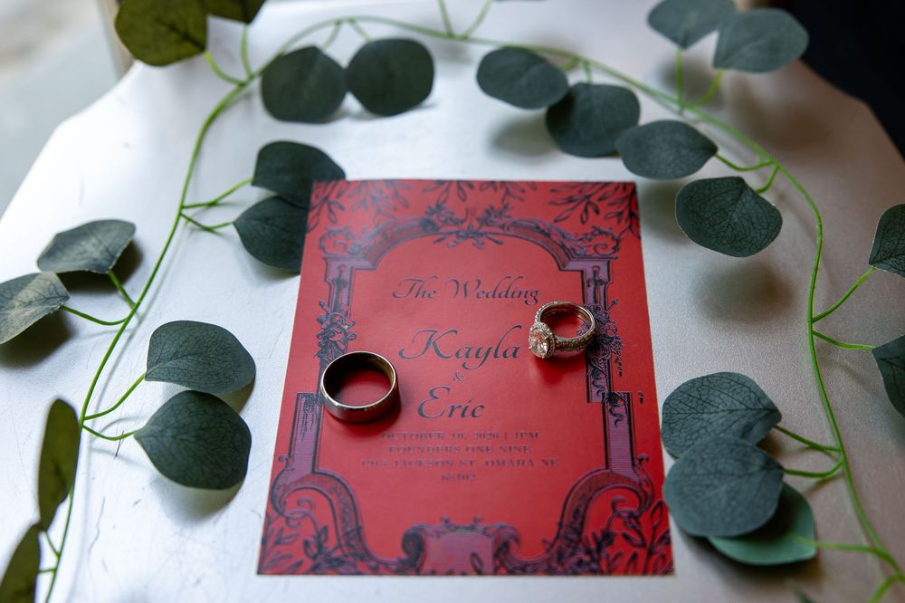 Red gothic-style wedding invitation for Kayla and Eric with two wedding rings resting on top, surrounded by eucalyptus leaves.