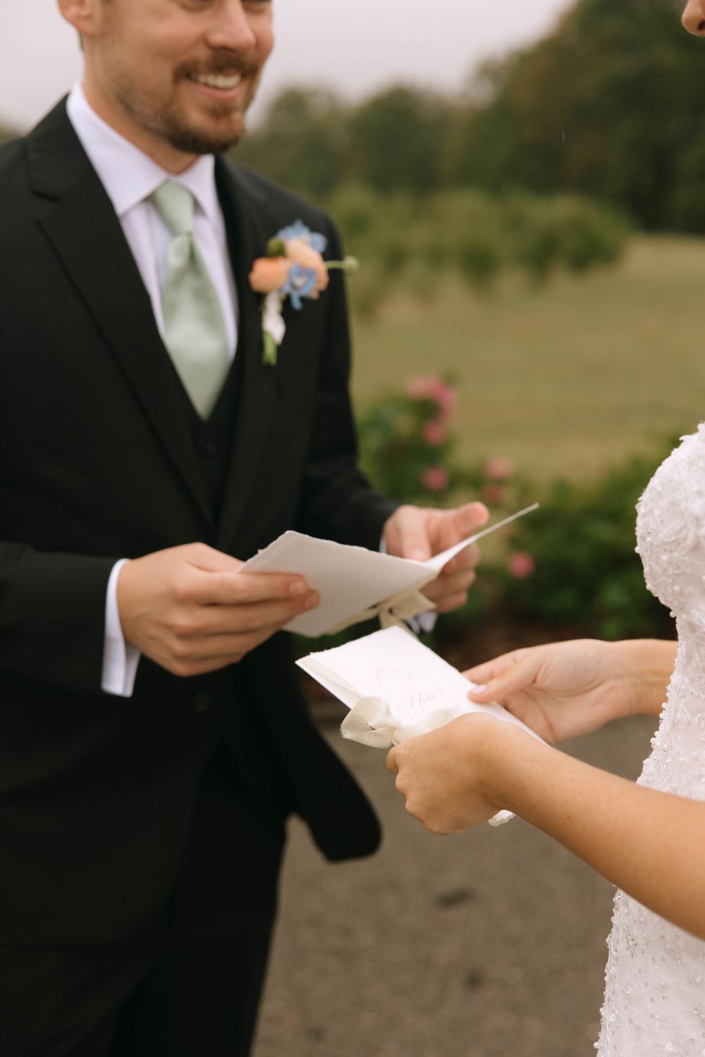 A smiling groom with a floral boutonniere reads a handwritten letter while the bride holds hers during a private moment.
