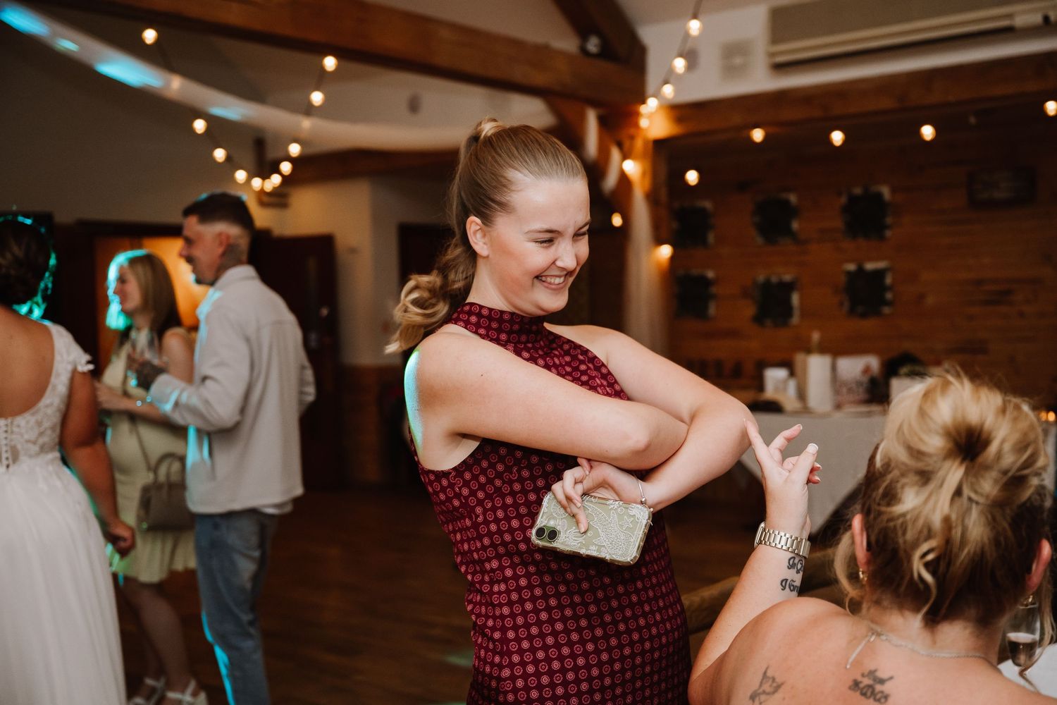 Woman in a burgundy patterned dress laughs while dancing at a wedding with string lights and guests in the background at Northover Manor