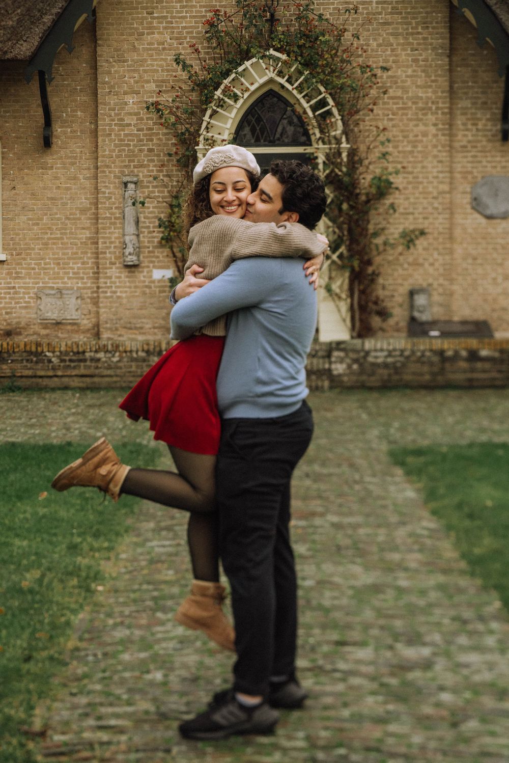 Man lifting woman in a joyful embrace outside a historic stone church.