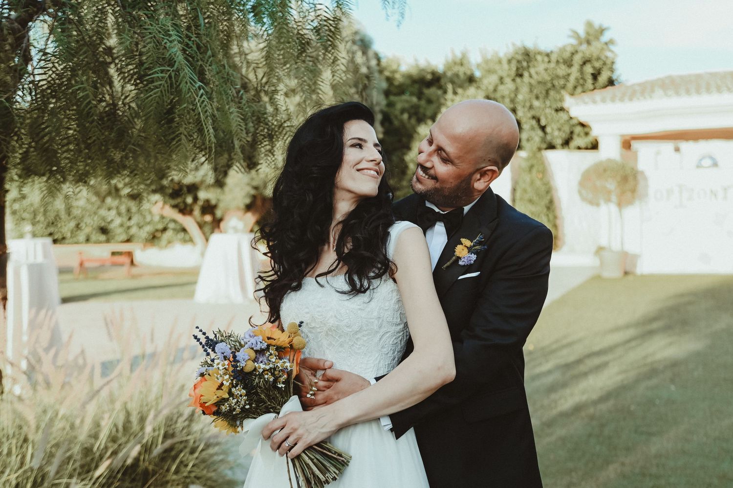 Black and white wedding photo of bride and groom gazing at each other outdoors among trees.