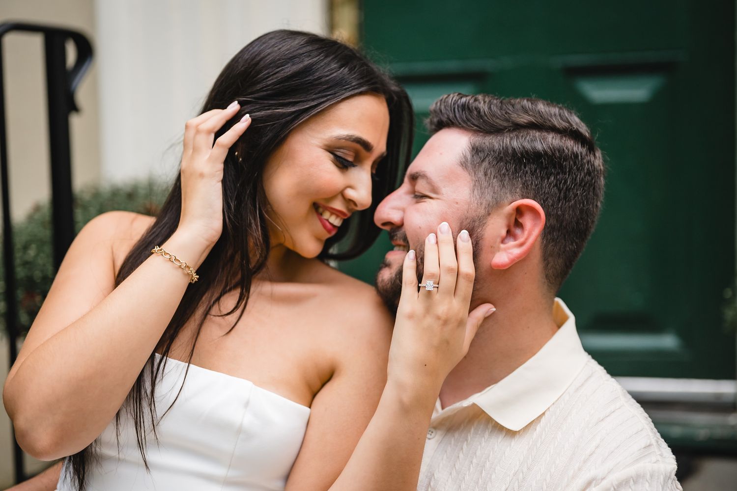 A joyful couple shares an intimate moment, with the woman showing off her engagement ring outdoors.