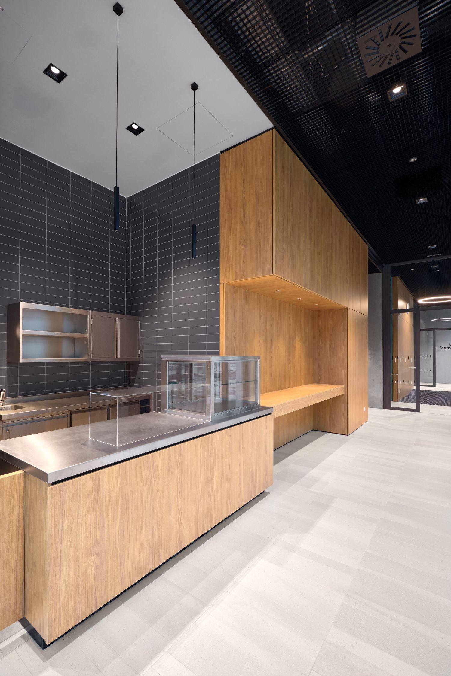 Modern interior with a glass-enclosed light well, pale tile flooring, wood paneling and bench, concrete wall and a dark ceiling.