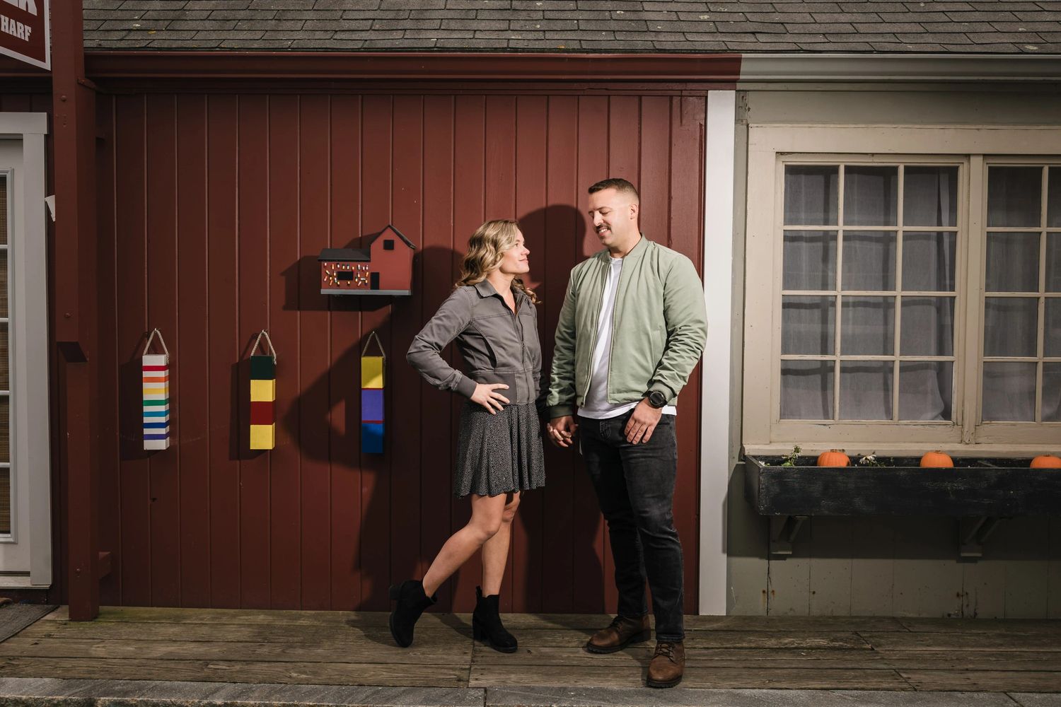 Couple standing together on a porch, looking at each other and smiling.  Engagement at Rockport Harbor, Rockport, MA