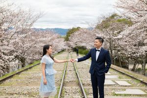 Couple holding hands and walking along old railway tracks lined with blooming cherry blossom trees during a spring engagement photoshoot.