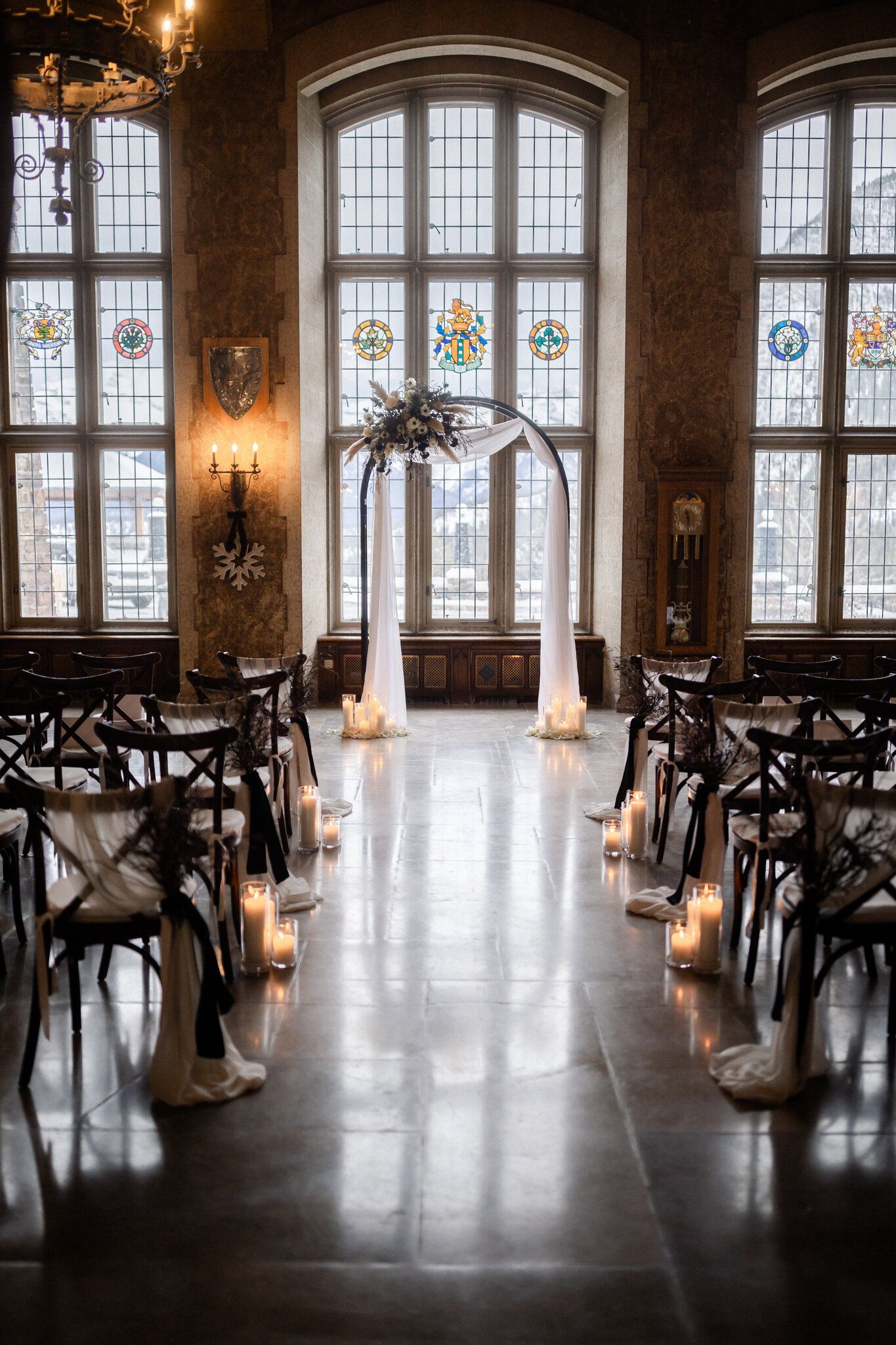Empty Fairmont Banff Springs ceremony hall with candlelit aisle, draped arch and stained-glass windows