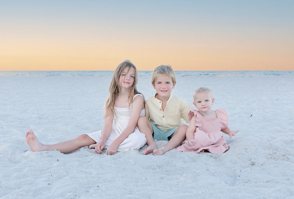 Three grandchildren sitting together on the sand at sunset