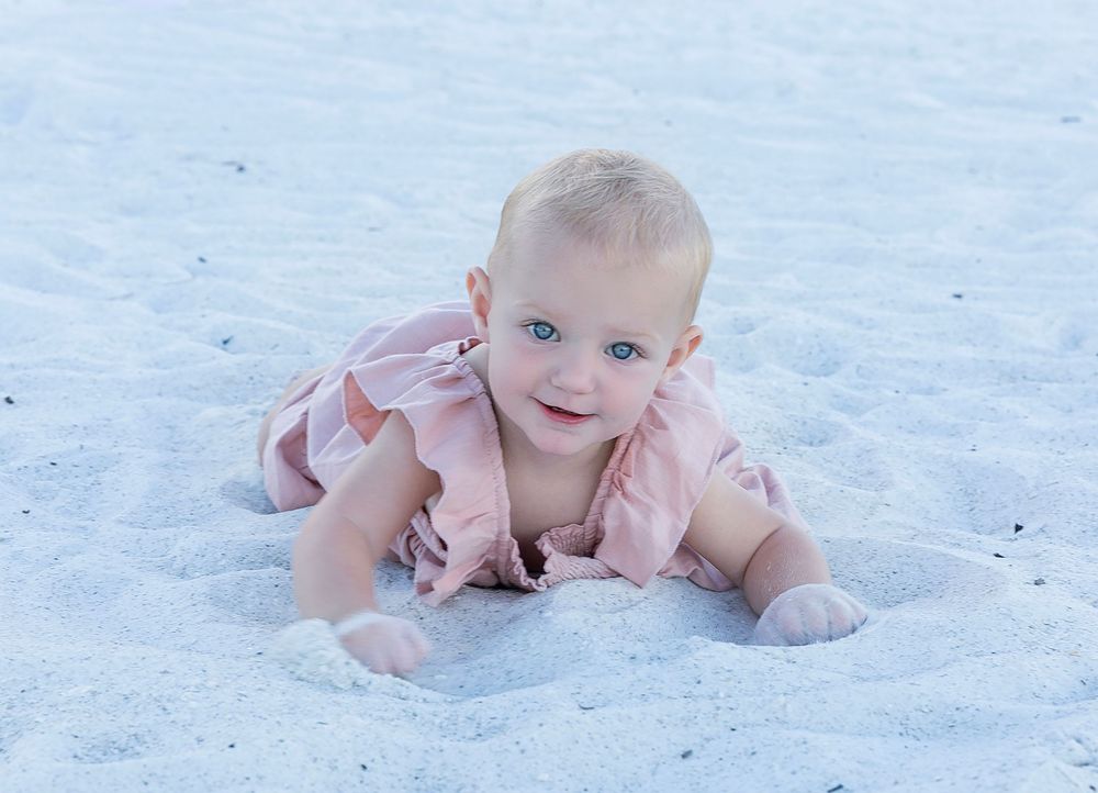 Baby girl in a pink dress crawling on the white sand