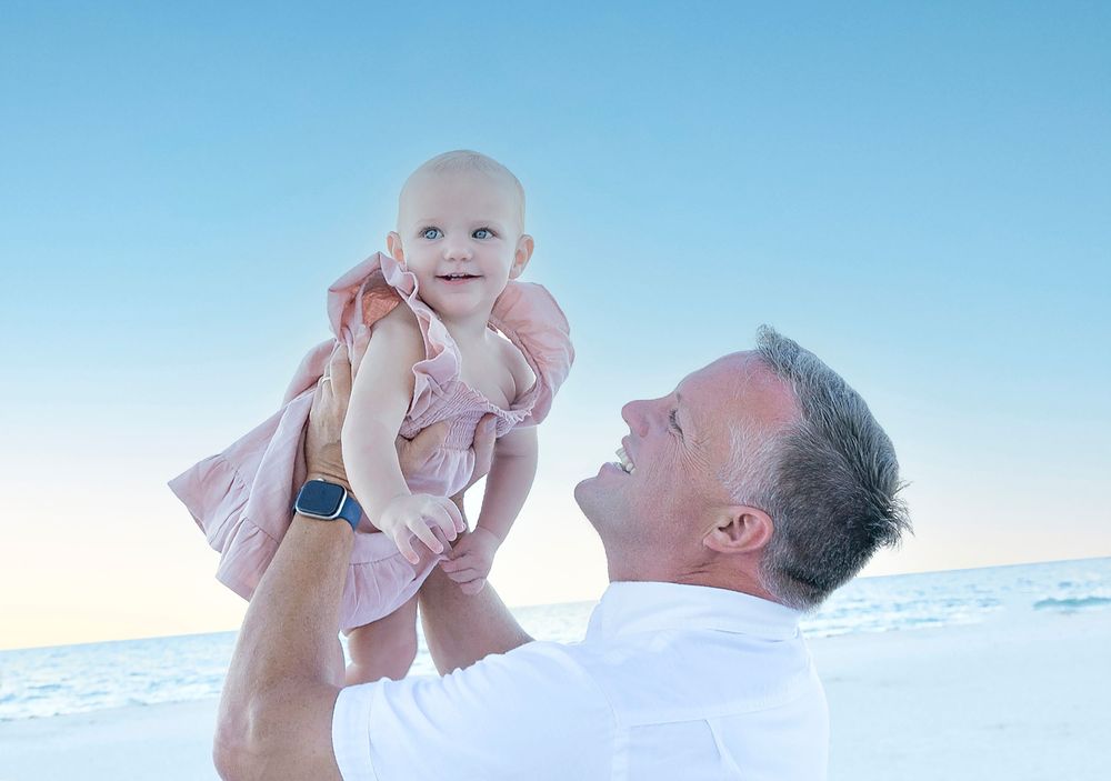 Grandpa lifting his baby granddaughter toward the pastel sky