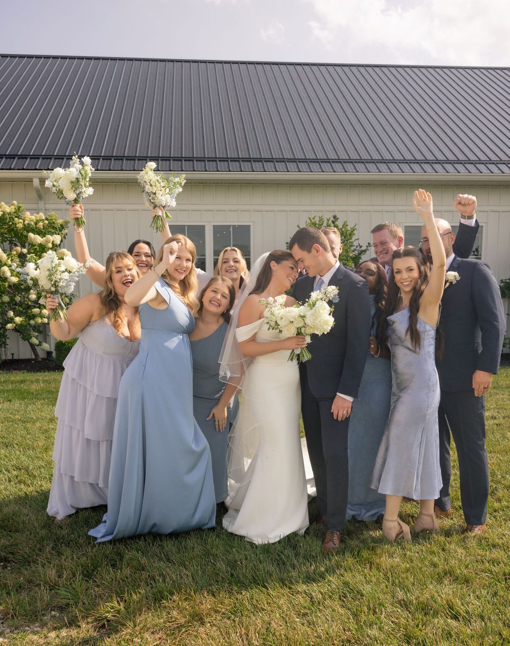 Bridesmaids in mix-and-match blue and lavender dresses in front of the white farmhouse at Magnolia Hill Farm