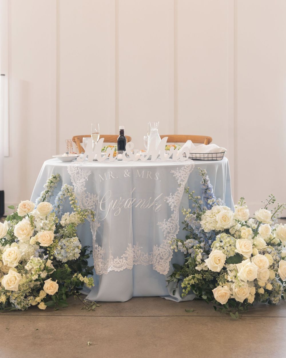 Elegant wedding sweetheart table with blue linen, white floral arrangements, and Mr. & Mrs. signage.