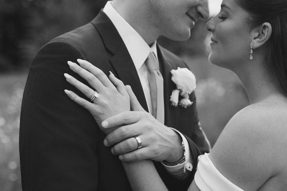 Black and white wedding photo of bride and groom embracing closely, showcasing diamond engagement ring and wedding band.