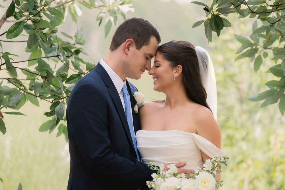 Bride and groom share a romantic moment under lush green branches on their wedding day.